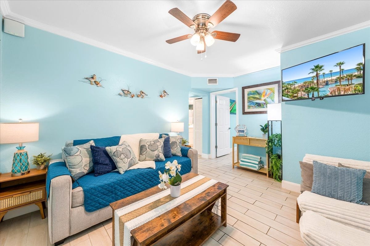 Clearwater Beach Suites 102: Settle into the cheerful coastal living room with comfortable seating, a sofa sleeper, ceiling fan, and wall-mounted TV.