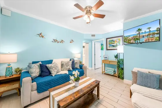 Settle into the cheerful coastal living room with comfortable seating, a sofa sleeper, ceiling fan, and wall-mounted TV.