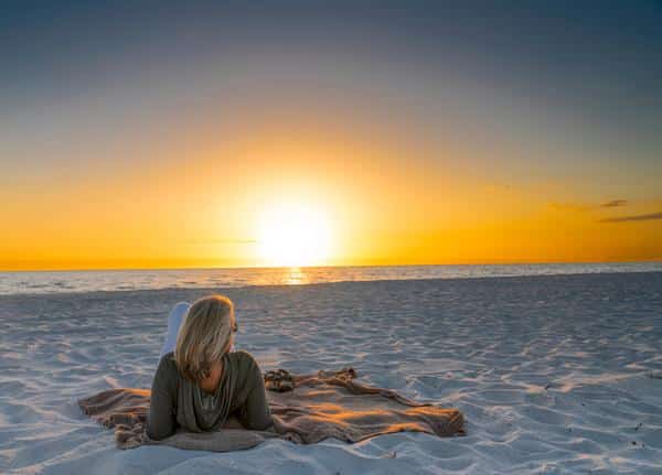 woman laying on blanket at the beach looking at the sunset