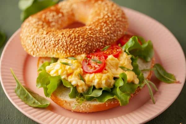 bagel with scramble eggs lettuce and tomatoes in a plate