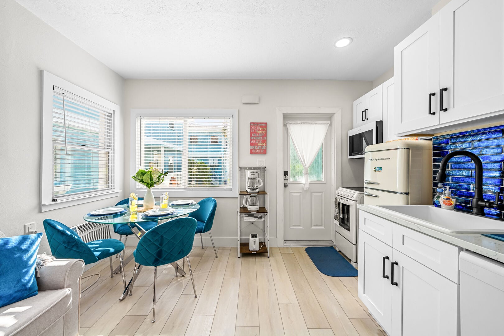 Cook in beach-house style — a complete kitchen with full oven and range, retro refrigerator, microwave, dishwasher, quartz counters and a cobalt glass-tile backsplash, opening straight onto the dining nook.