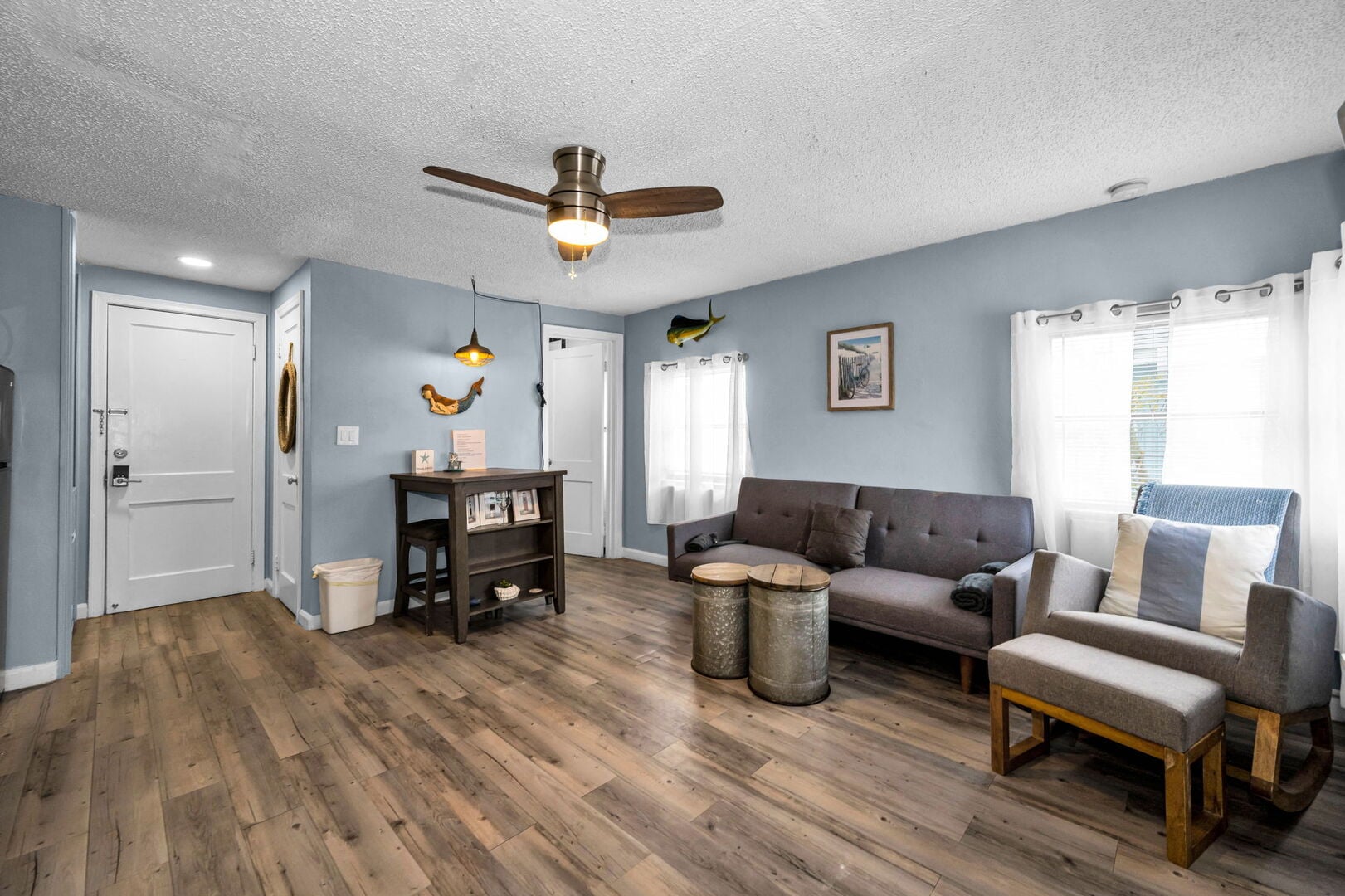 A cozy studio living space with a comfy sofa and armchairs, coastal artwork, and easy access to the ensuite bathroom — just two short blocks from the beach.